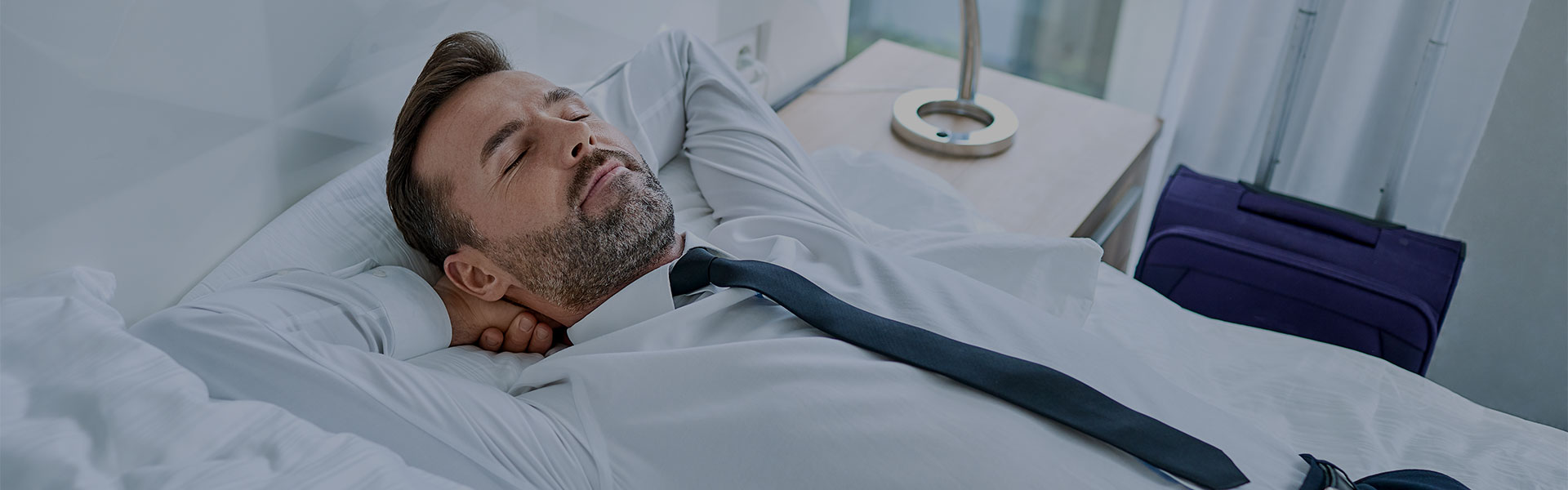 man resting contentedly on bed with arms behind his head